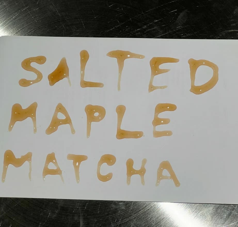 “Salted Maple Matcha” hand-lettered in syrup on a white surface
