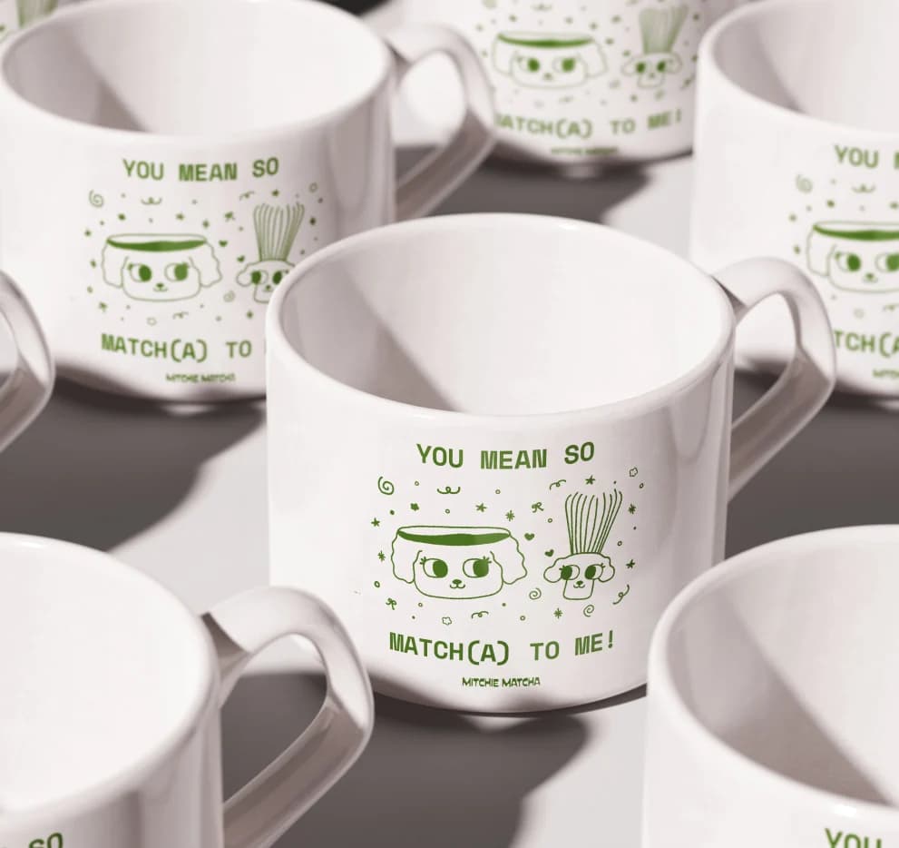 White mugs printed with “You mean so matcha to me!” and a green illustration
