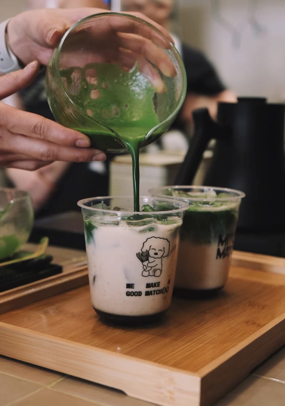 Matcha poured into a branded cup of milk on a wooden tray