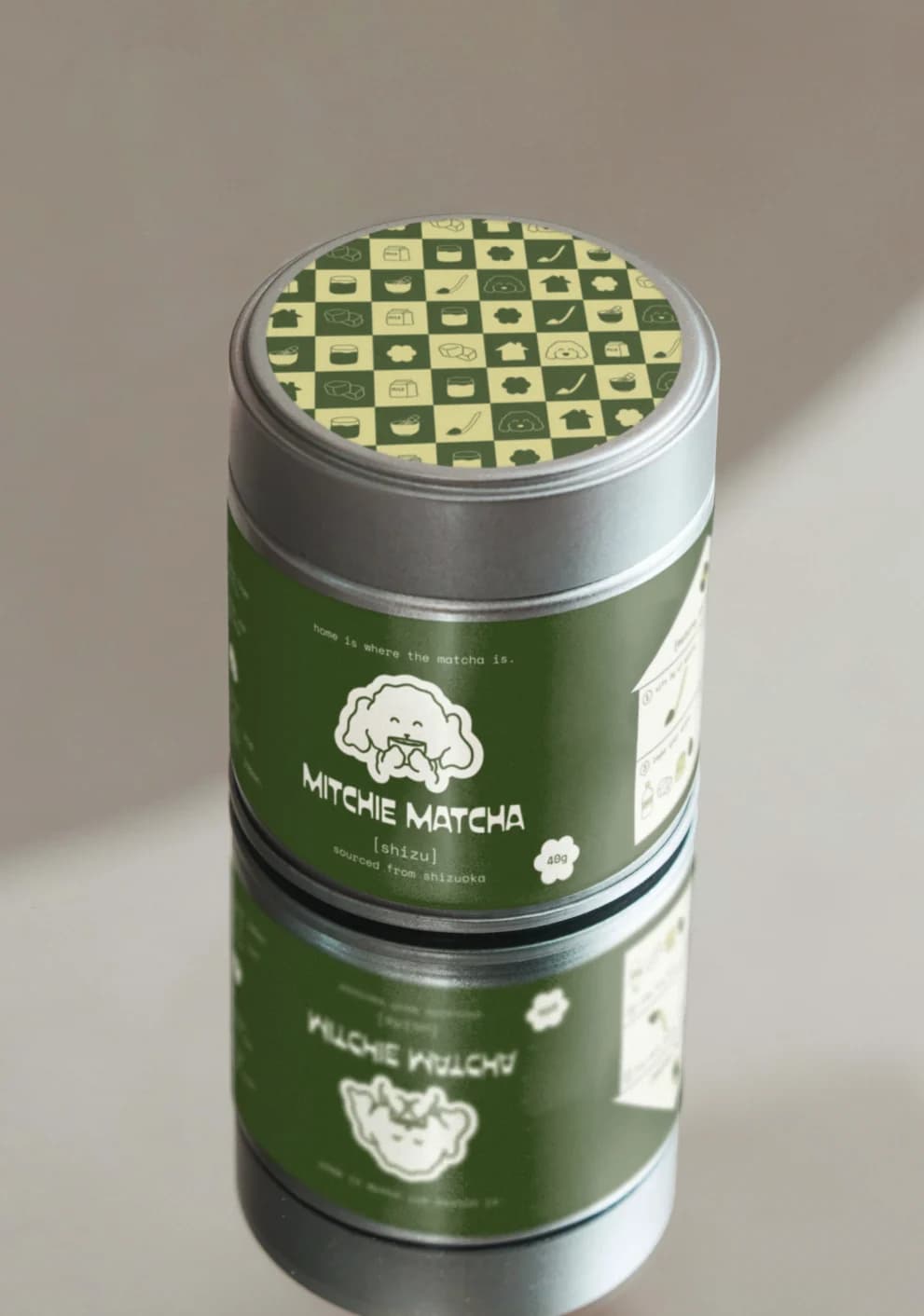 Mitchie Matcha tin with a green label and checkered lid, reflected on a glossy surface