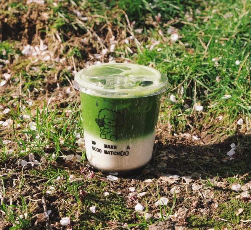 A Mitchie Matcha iced matcha latte cup sitting in the grass